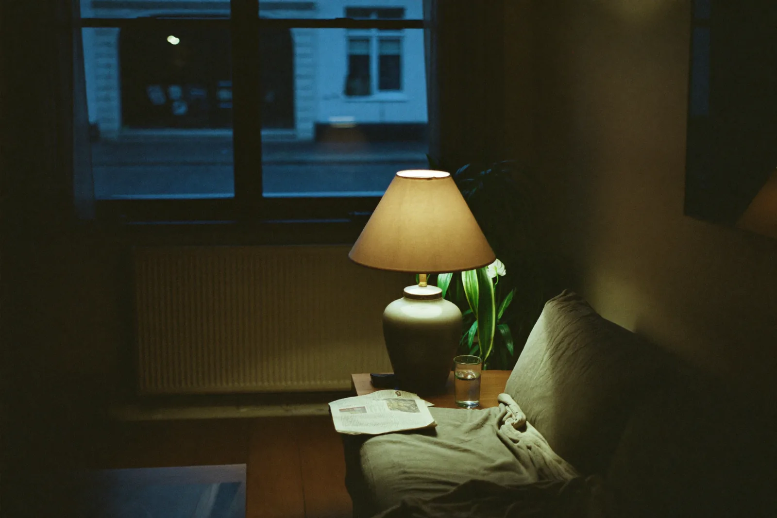 Stille woonkamer in de avond met één brandende schemerlamp en een donkere straat achter het raam