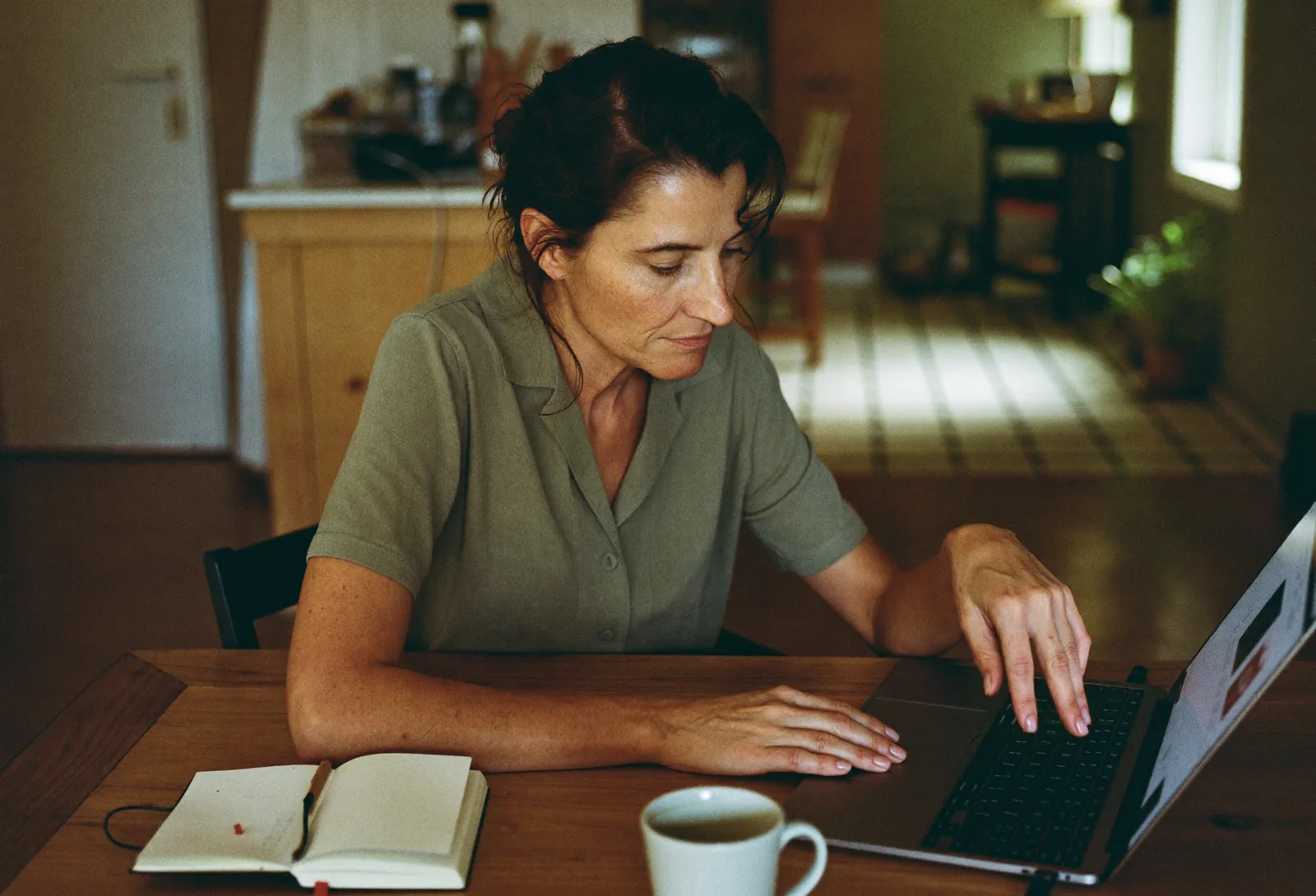 Vrouw rekent aan een keukentafel met een laptop, notitieboek en koffie iets door