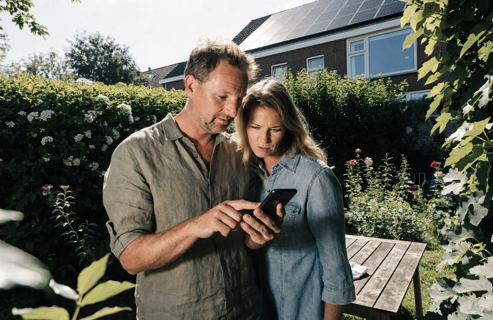 Stel bekijkt bezorgd de energierekening op een telefoon in de tuin