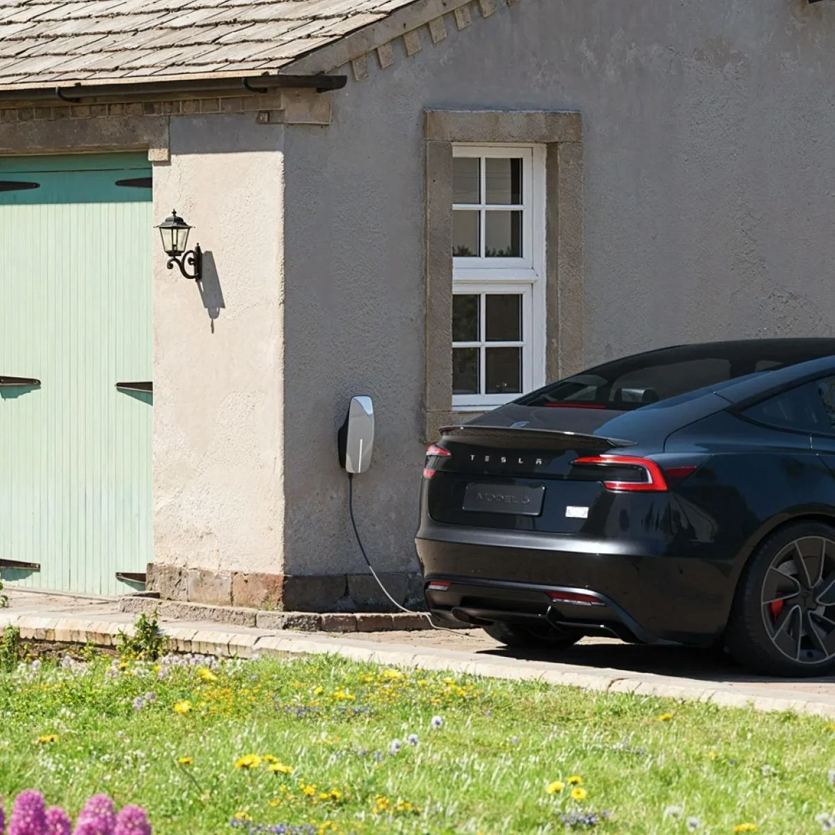Laadpaal aan de gevel van een woning met een auto op de oprit